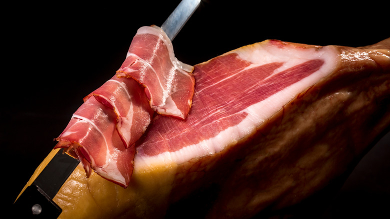 prosciutto being sliced with a long thin knife