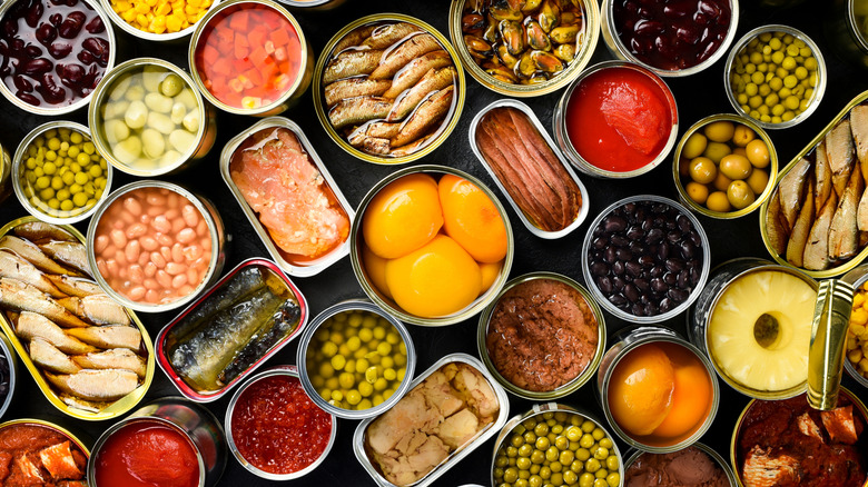 Many opened cans of food on a table, including sardines, peas, beans, pineapple and more