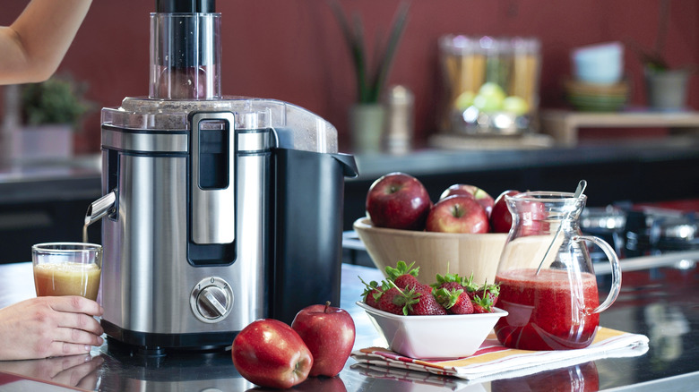Person using a cold press juicer to juice apples and strawberries