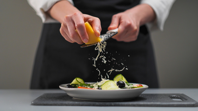 Person grating cheese over salad