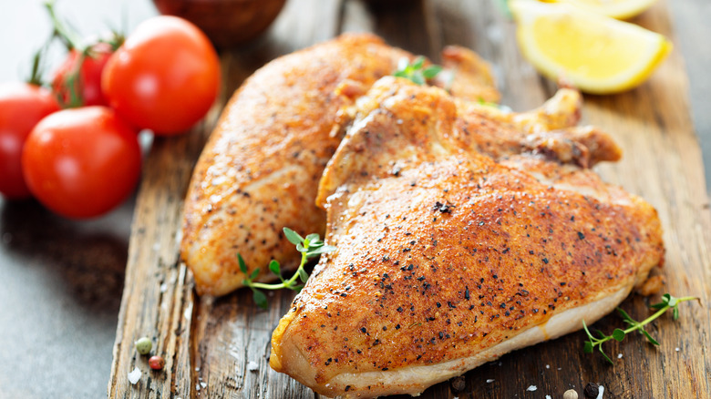 Two grilled bone in chicken breasts on wooden board