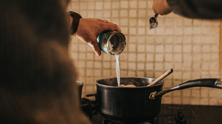 man pouring coconut milk into pot