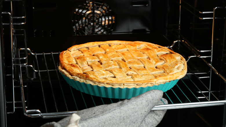 hand in oven mitt sliding rack out to check on lattice-top pie