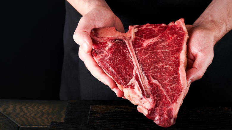 butcher holding large raw t-bone steak