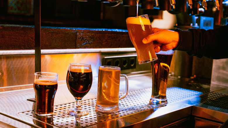 Bartender's hand filling pint of IPA at tap with 4 other styles in glasses below