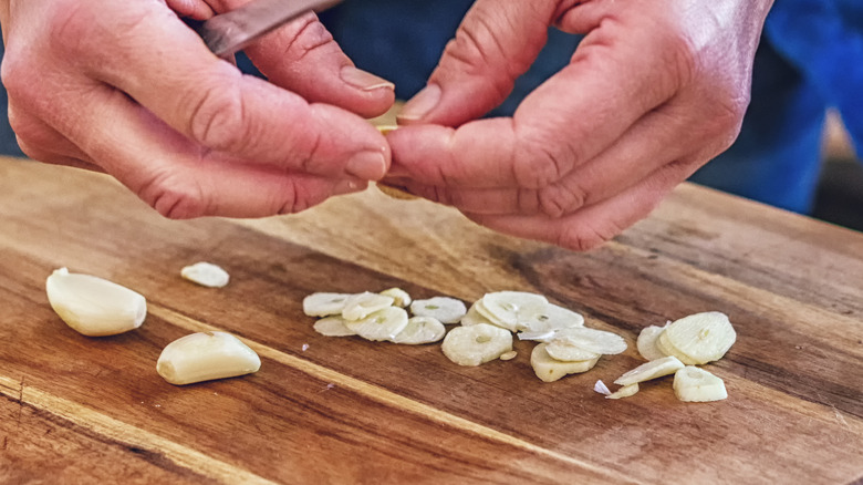 hands slicing garlic on board