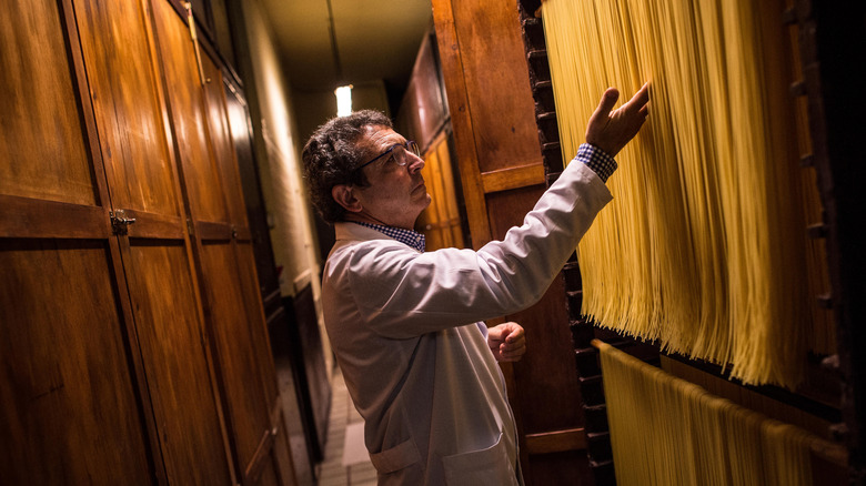 Man touching spaghetti, air-drying in a wooden cabinet