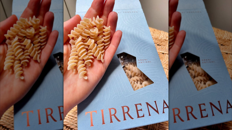 A hand holding bronze-cut pasta over a product box