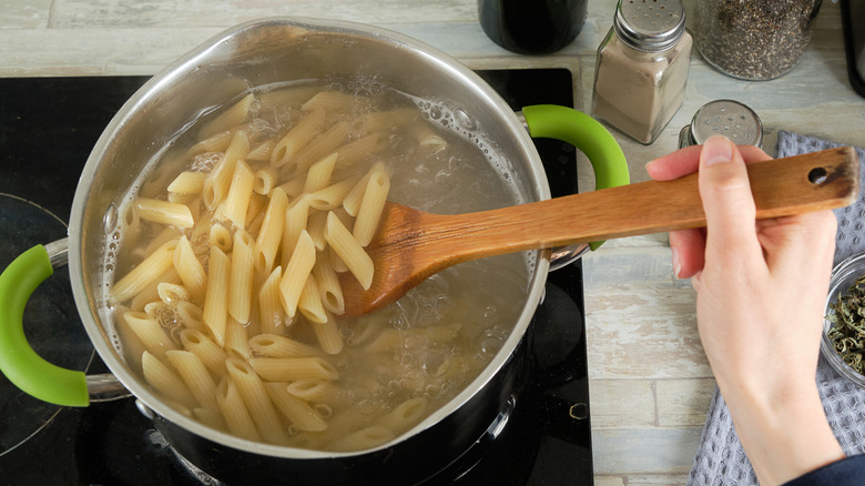 A pot of penne pasta being hand-stirred as it cooks