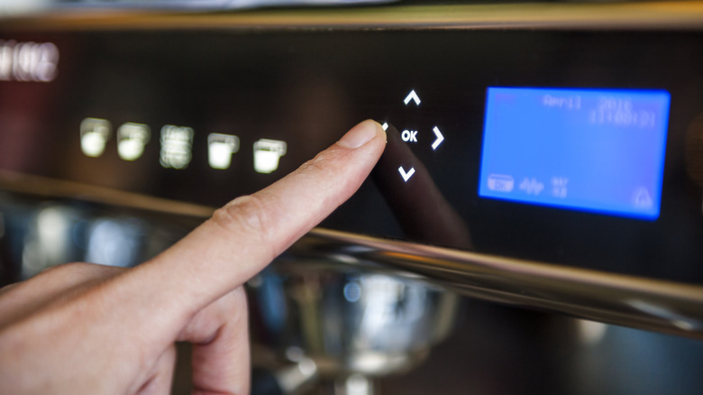 A person pushes a coffee settings button on an appliance.