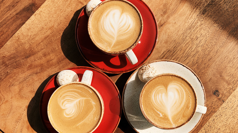 Three lattes with art in the foam are sitting on a wooden table.