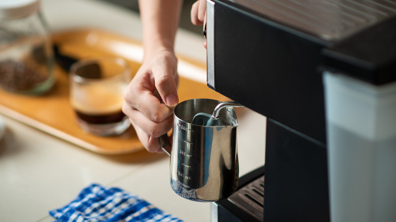 A person is steaming milk in a metal pitcher.