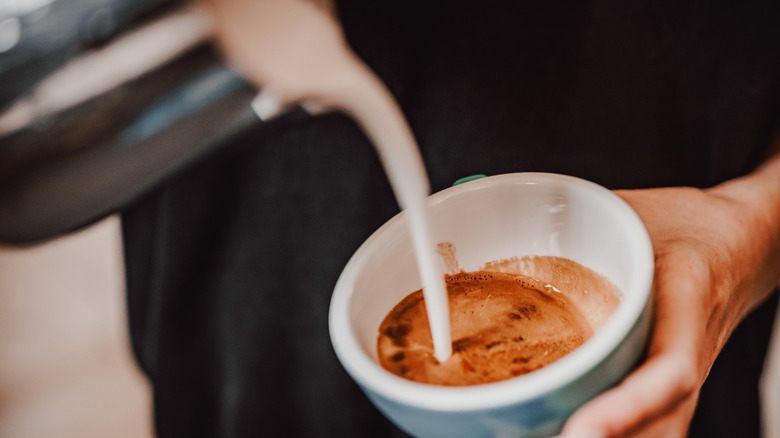 A person pours steamed milk in a coffee mug.