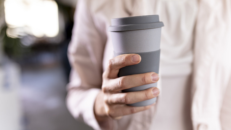 A woman holds a gray reusable coffee mug.