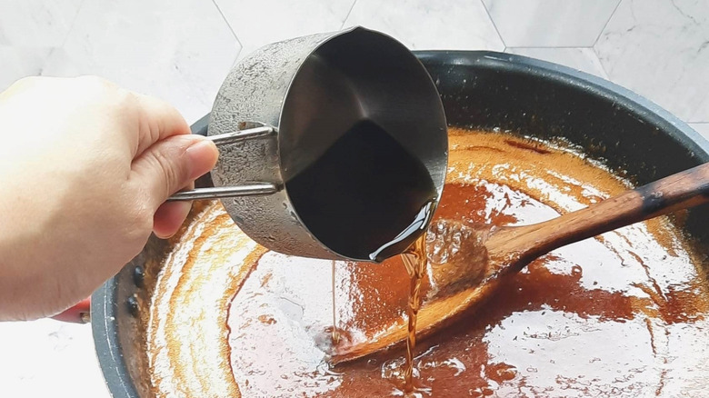 a chef building a sauce in a pan by adding a cup of liquid straight into a bubbling sauce