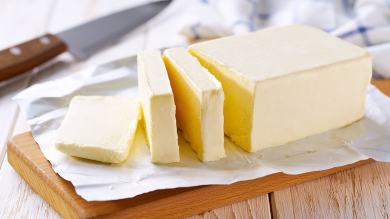 a block of fresh butter placed on a wooden board with several thick slices and a knife in the back