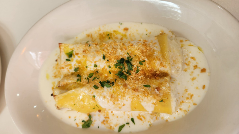 top view of a plate with cannelloni topped with béchamel sauce and a sprinkle of breadcrumbs and parsley