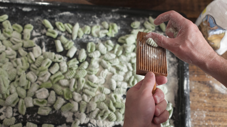 Person making green cavatelli rolling pasta pieces with a grooved wooden tool