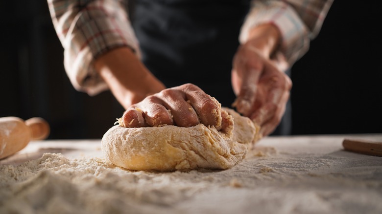 Person in apron and rolled up shirtsleeves kneading pasta dough