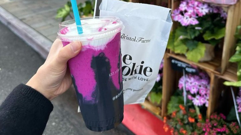 Customer holding juice and cookie in front of flowers outside Bristol Farms