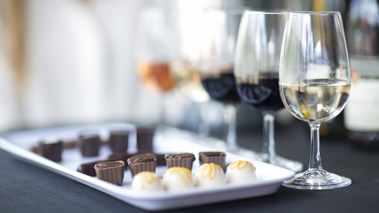 assorted chocolates lined on a white plate with wine glasses in the front set up for a wine tasting