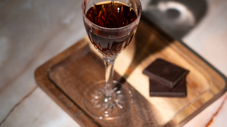 glass of sherry placed on a wooden board next to two pieces of dark chocolate bar