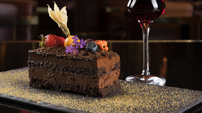 layered chocolate cake topped with edible flowers and various fresh fruit and glass of red dessert wine