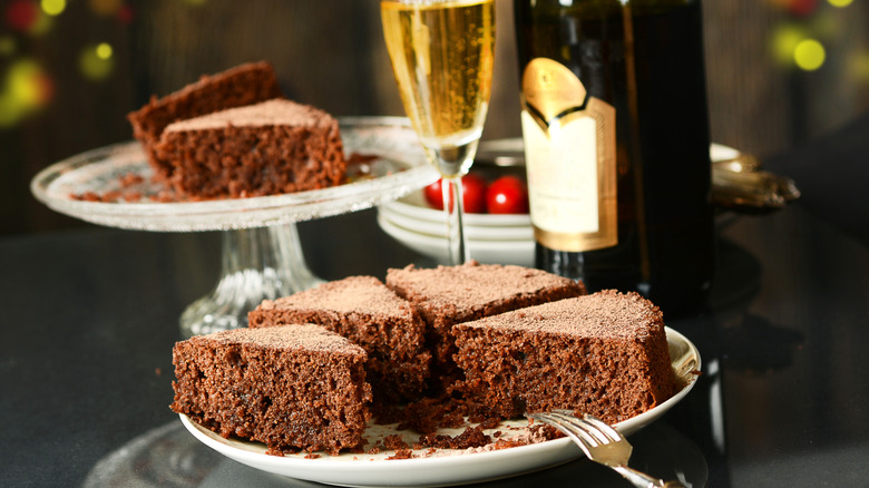 sliced chocolate cake assembled on a plate with a champagne glass and bottle in the background