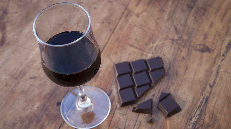 a glass of red wine on a wooden board with a block of chopped dark chocolate