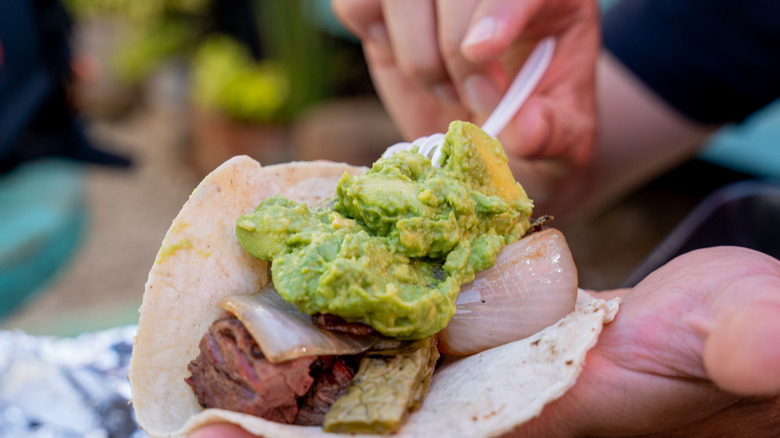 person spooning avocado onto taco