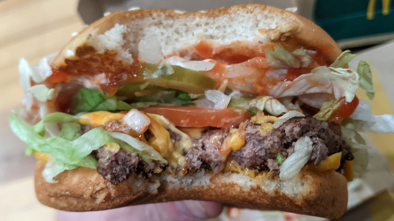 Quarter Pounder Deluxe with a bite taken out of it to show lettuce, tomatoes, pickles, and burger inside