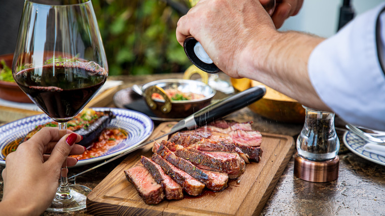 Hand holding red wine by steak