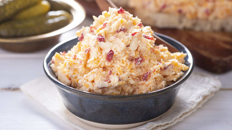 Bowl of homemade pimento cheese with pickles in background