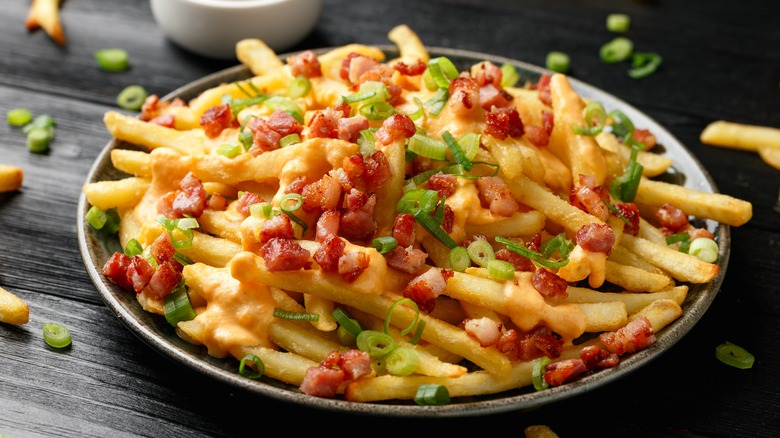 Bowl of loaded french fries with bacon, cheese, and scallions