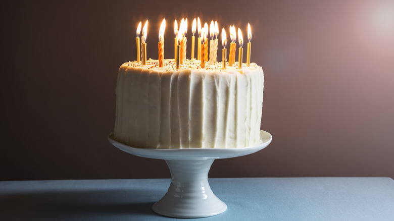 An iced birthday cake on a stand with candles