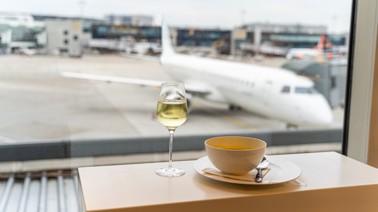 Glass of white wine, a bowl of soup with a spoon near window with a view to a white airplane in departure launch cafe of an airport