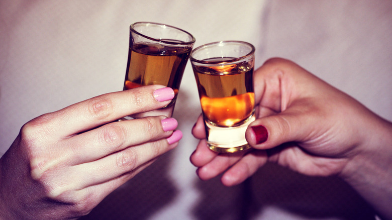 Close-up of two hands holding whiskey shots