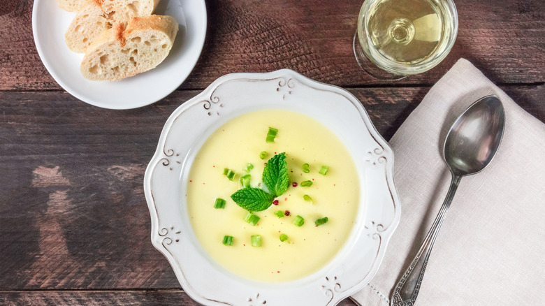 Potato soup on a wooden table beside wine, a spoon, and bread