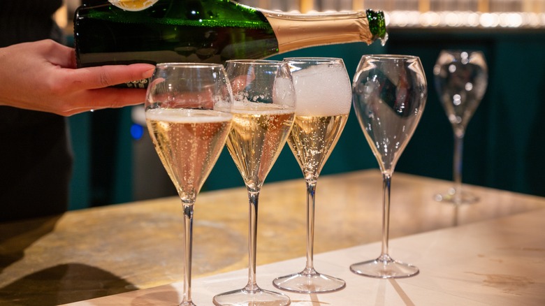 hand pouring sparkling wine into a line of glasses