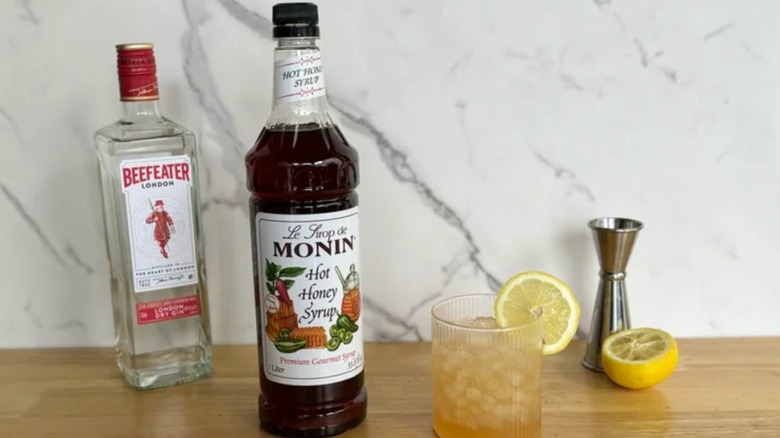 Monin hot honey flavored syrup on a table with a bottle of Beefeater and glasses