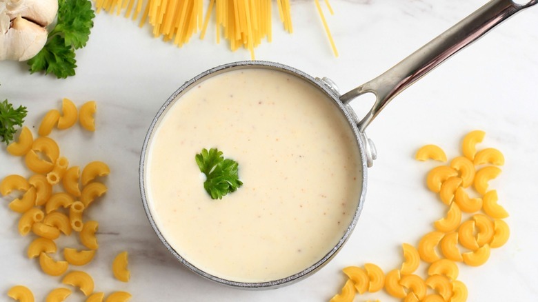 creamy sauce in a pan with dried macaroni and spaghetti on the table