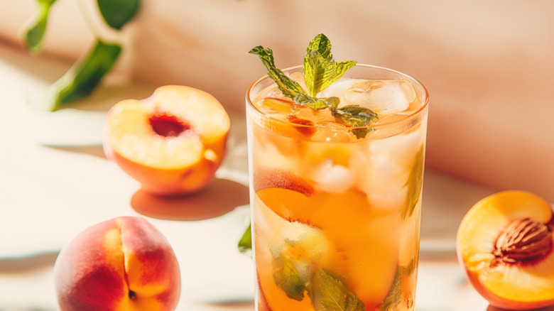 A glass of iced tea with peaches in and around it