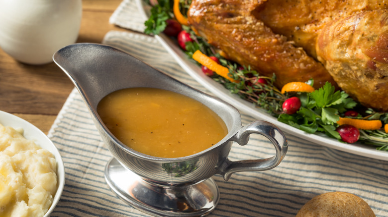 A gravy boat next to a cooked turkey and bowl of mashed potatoes