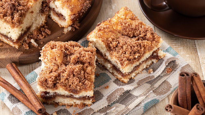 two squares of coffee cake on a linen with cinnamon sticks