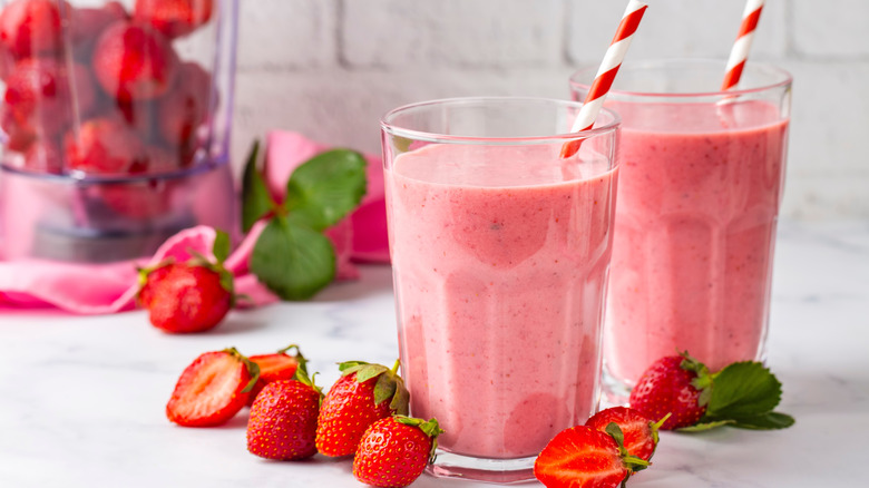 Fresh strawberry smoothies with striped red straws and sliced strawberries