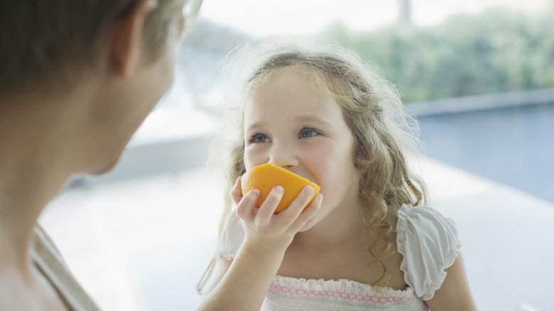 young girl biting an orange 