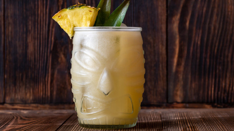 Frozen painkiller cocktail in a glass tiki mug against a dark background