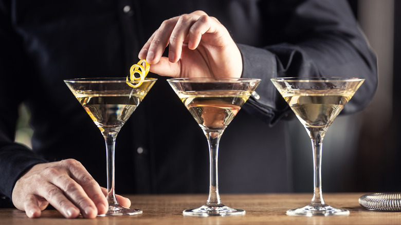 Hand adding lemon peel to martini