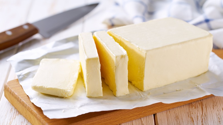 Block of butter on a wooden cutting board cut into slices