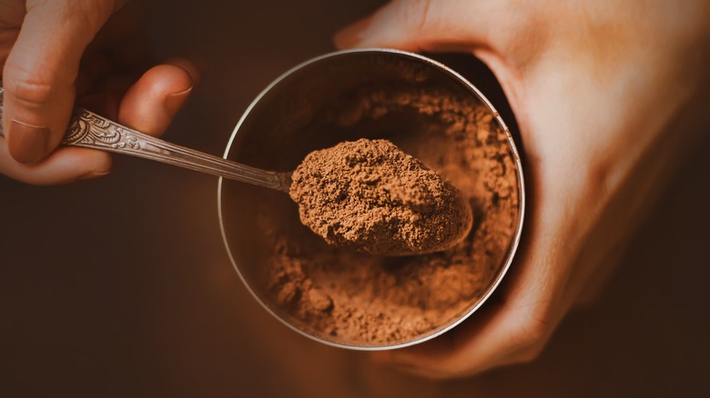 A person using a spoon to scoop out cocoa powder out of a container